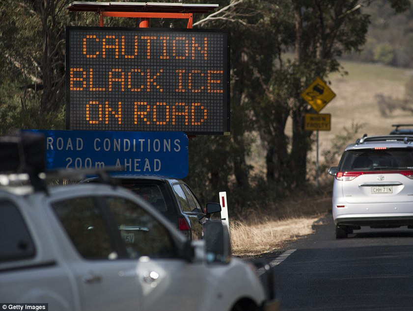 Cars driving on road next to a sign that reads: Caution black ice on road